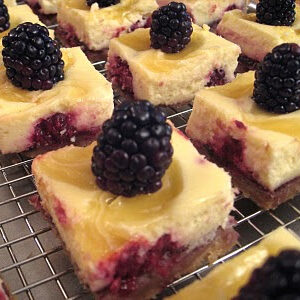 lemon blackberry cheesecake bars on a wire rack.
