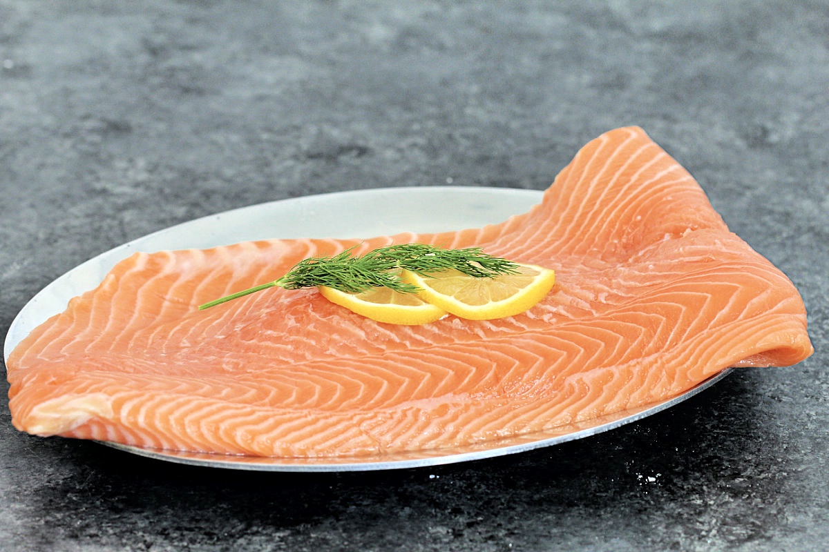 Large piece of salmon on a sliver plate with lemon slices and dill on top.