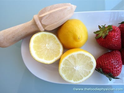 Lemons and strawberries on a plate with a wooden reamer.