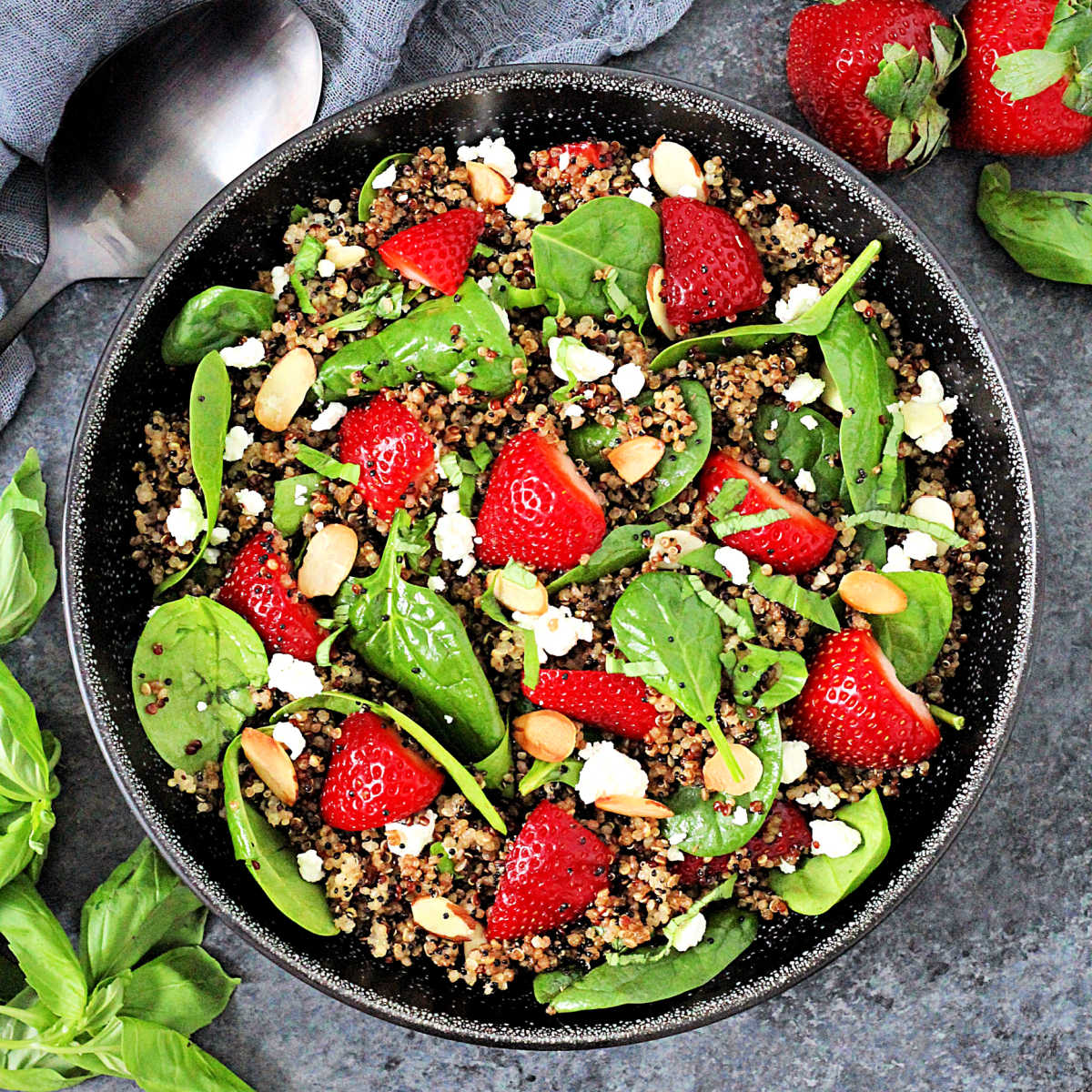 Quinoa salad with spinach and strawberries in a black bowl.