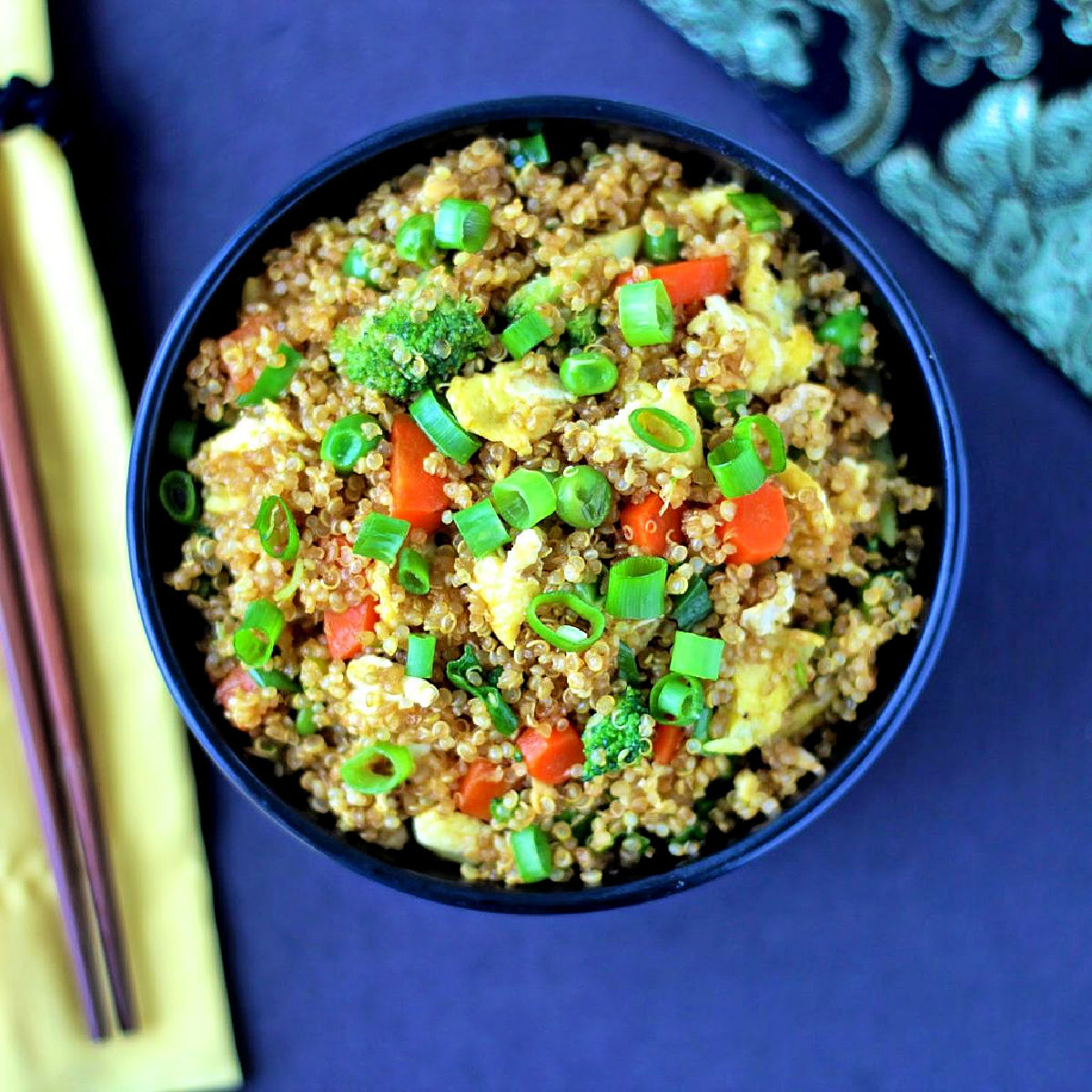 Quinoa fried rice in a black bowl with chopsticks and a yellow napkin nearby.