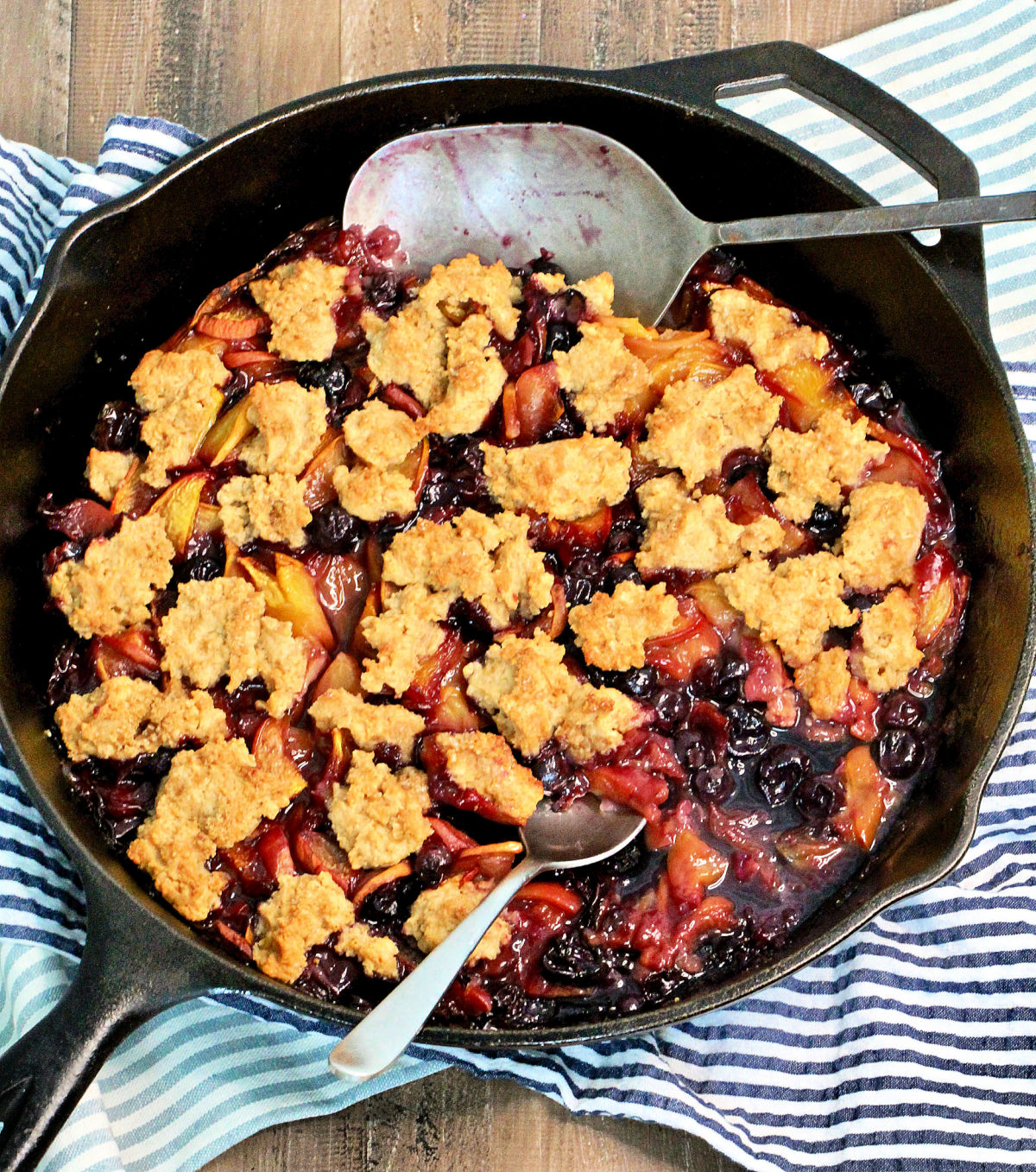 Healthy blueberry peach cobbler in a cast iron skillet with two spoons.