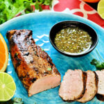 Cuban mojo pork tenderloin on a blue plate with mojo sauce in a black bowl.