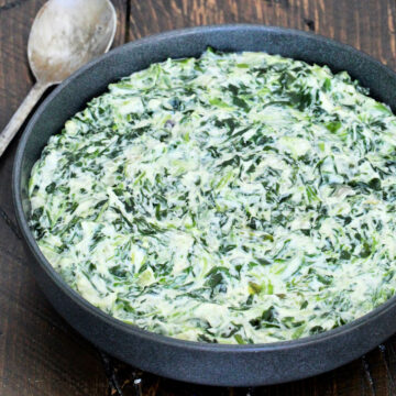 Easy creamed spinach in a black bowl on a wooden board with a metal spoon next to it.