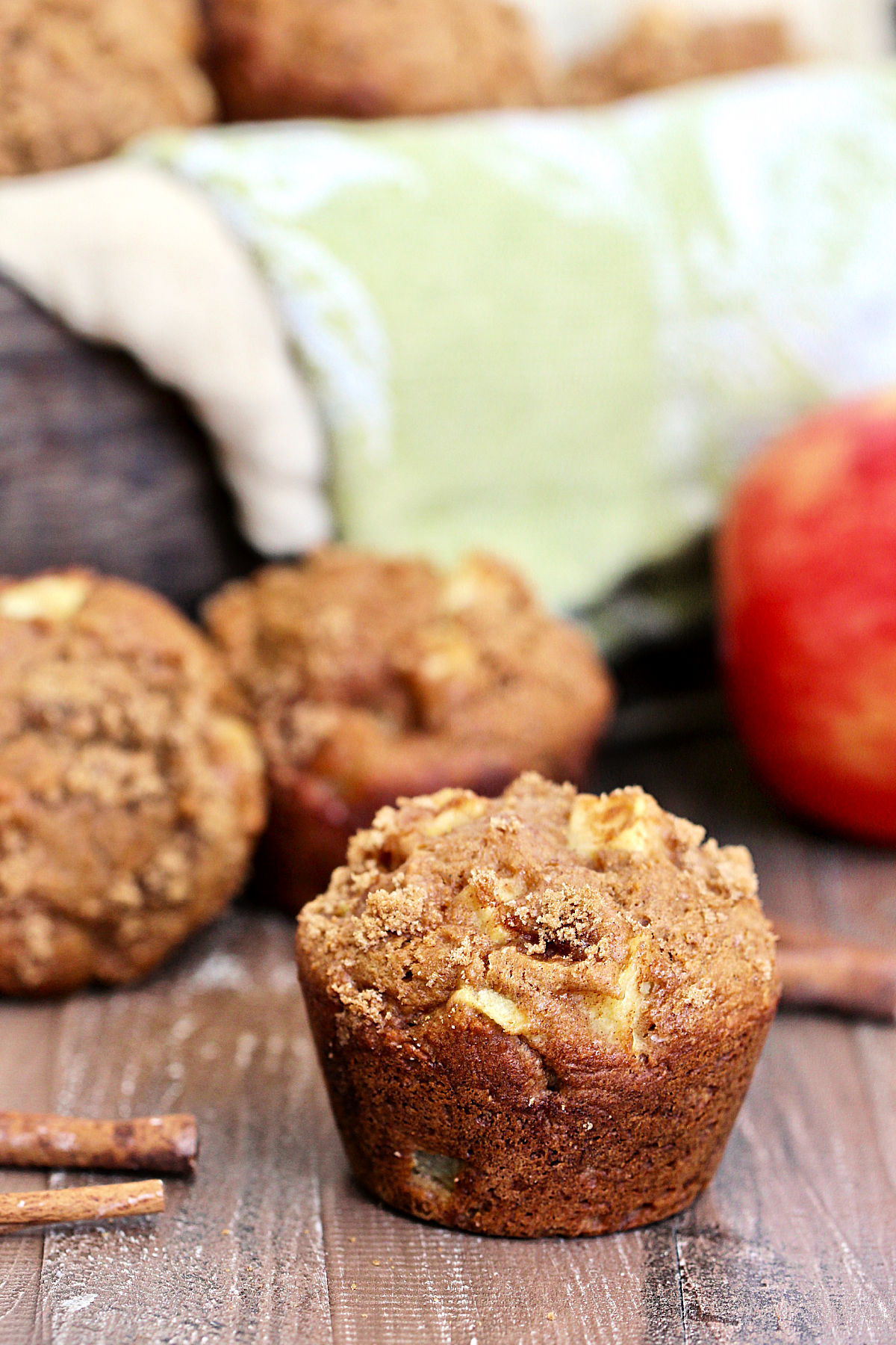 Single spiced apple muffin on a wooden board with more muffins in the background.