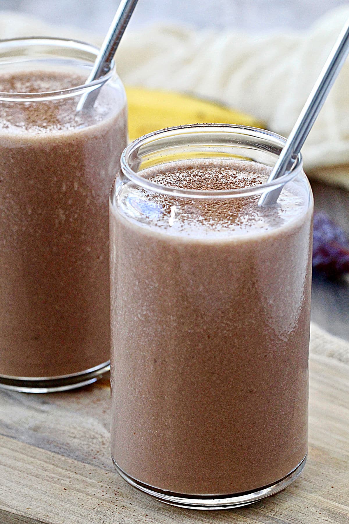 Two healthy chocolate smoothies in glasses with metal straws in them.