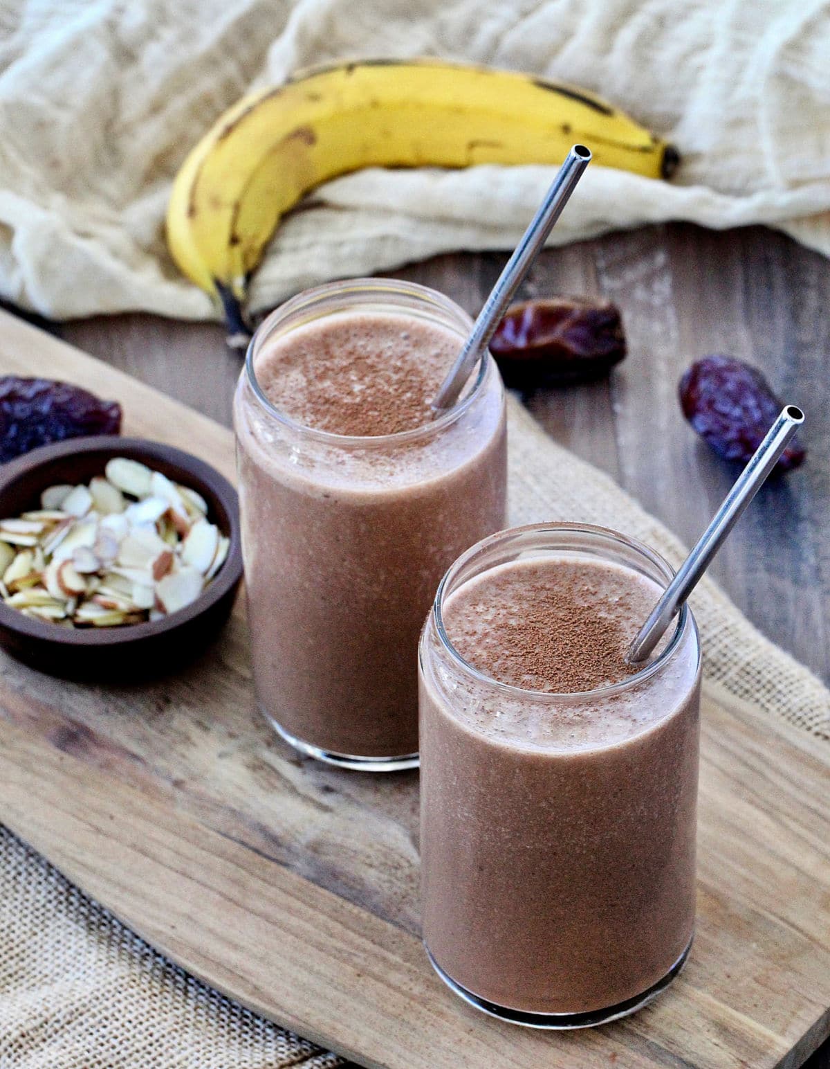 Two healthy chocolate smoothies in glasses with metal straws in them.