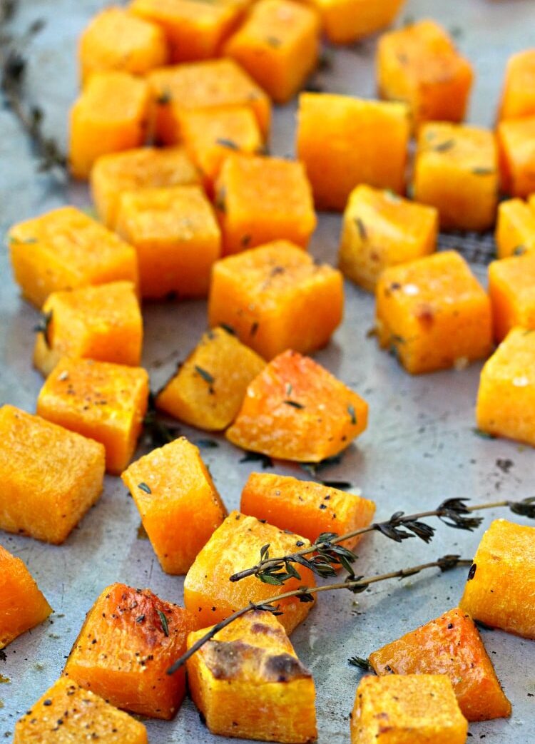 Diced butternut squash on a sheet pan with thyme leaves after cooking.