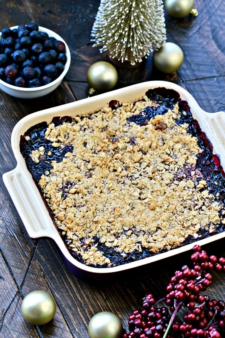 Angled photo of blueberry walnut crumble in a square baking dish with holiday decorations.