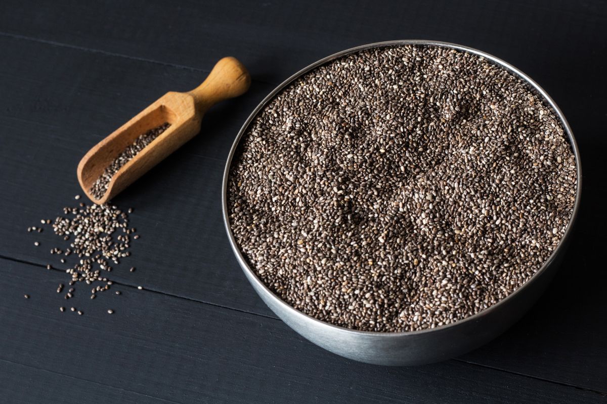 Chia seeds in a bowl with a wooden scoop next to it.