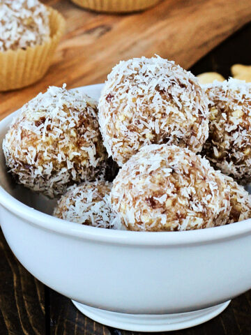 Coconut date balls in a white bowl with a wooden board in the background.