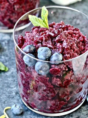 blueberry granita in a glass garnished with blueberries and mint sprig.