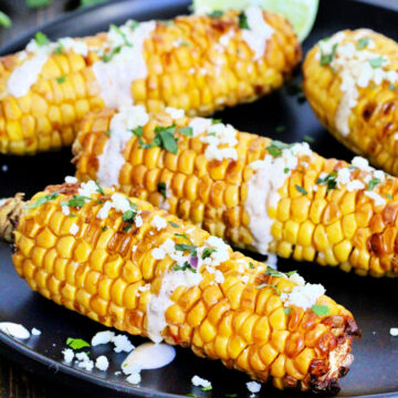 Four pieces of air fryer corn on the cob on a black plate.