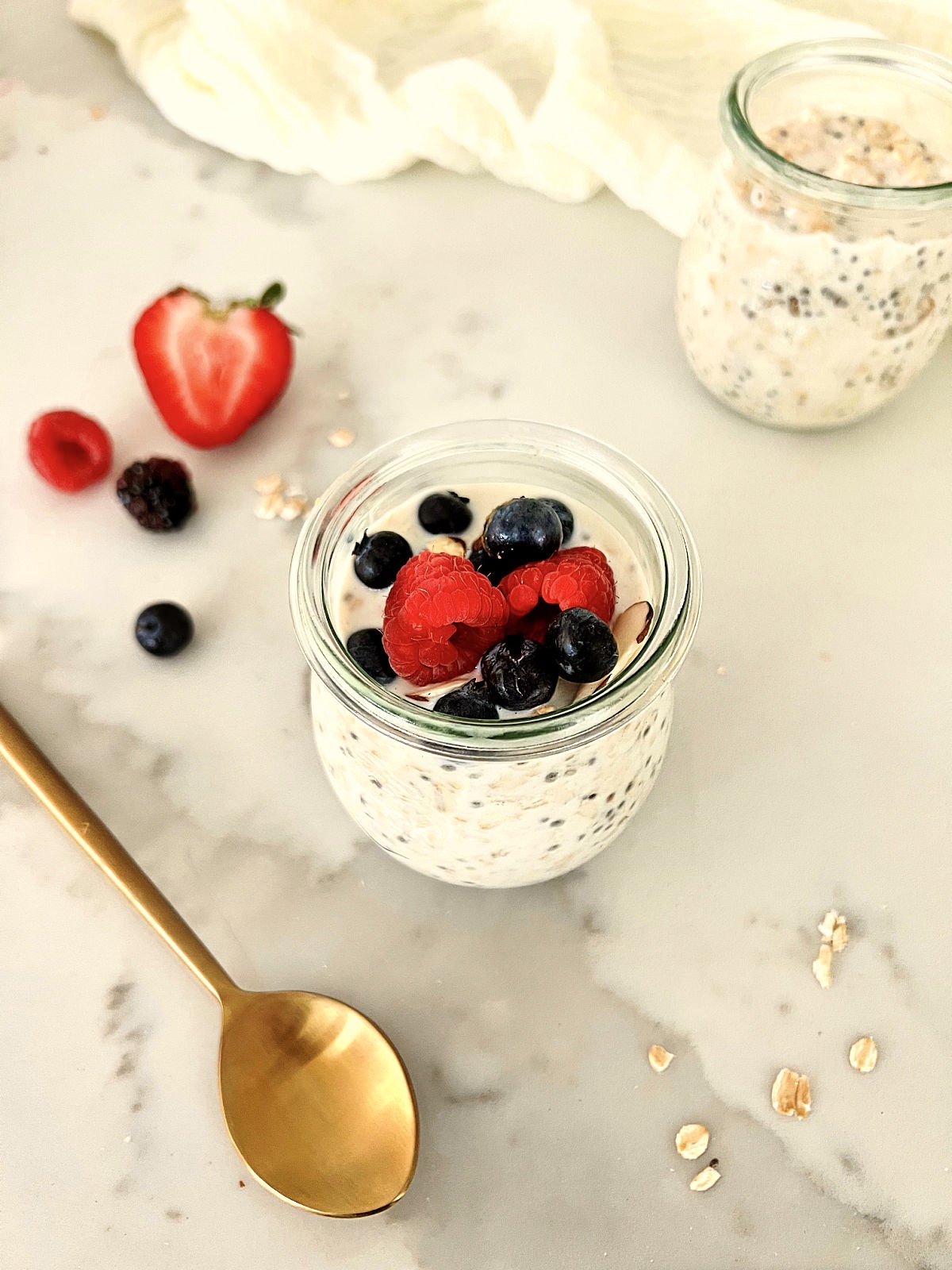 A jar of healthy overnight oats with berries and a gold spoon nearby.