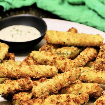 Air fryer zucchini fries on a plate with bowl of ranch dipping sauce and a green napkin.