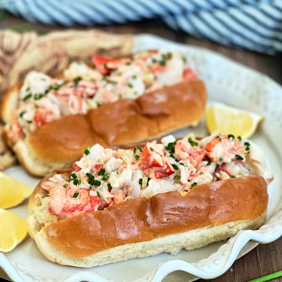 Two lobster rolls on a white plate with lemon wedges.