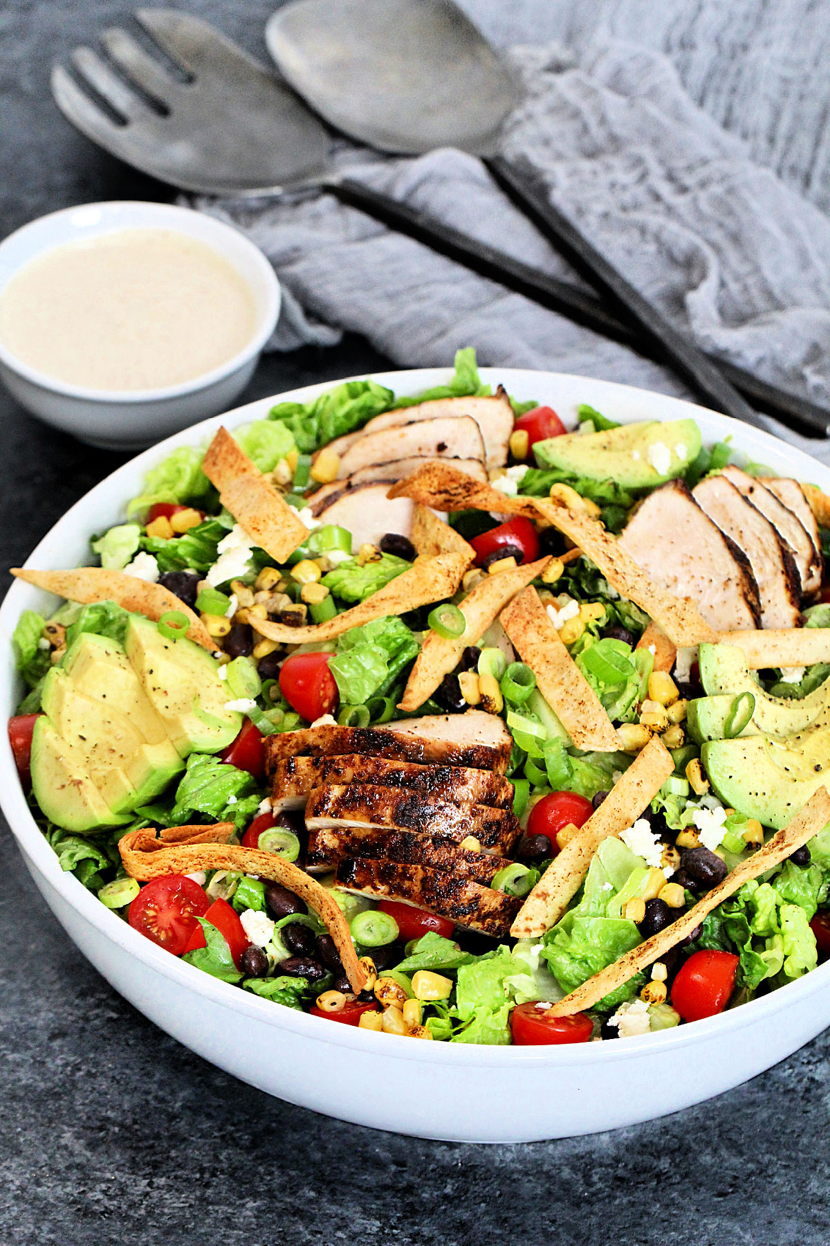 Santa Fe Chicken Salad in a white bowl with a small bowl of dressing on gray board.