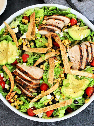 Overhead shot of santa fe salad in a white bowl with a small bowl of dressing on gray board.