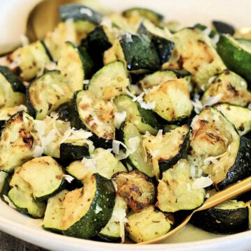 Air fryer zucchini in a white bowl with grated parmesan cheese on top.
