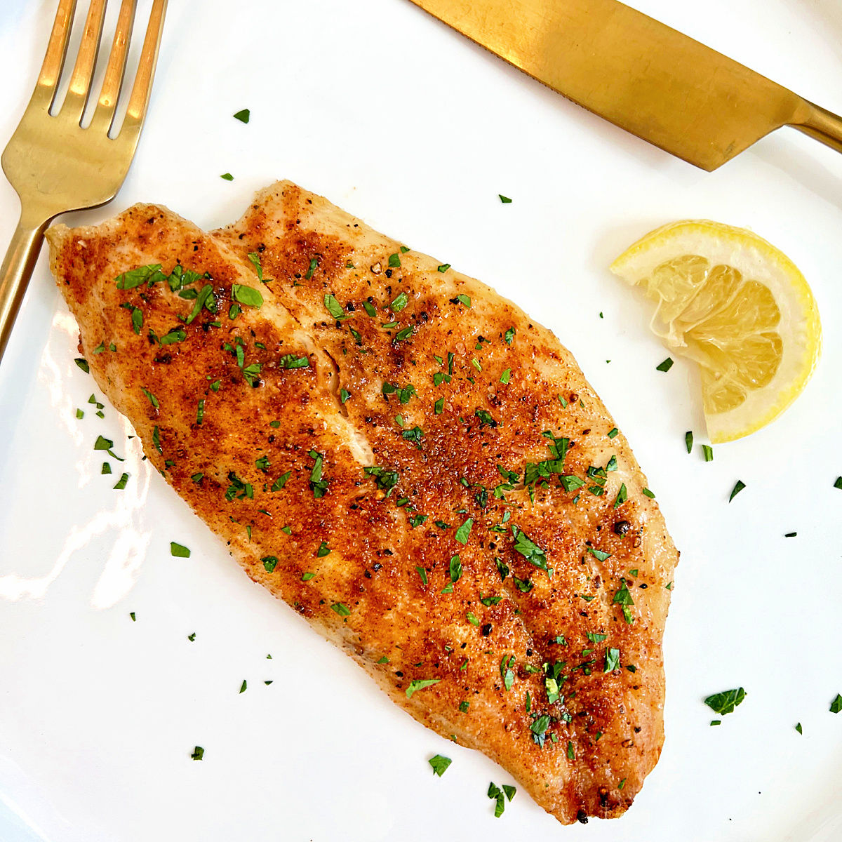 Piece of air fryer tilapia on a white plate.