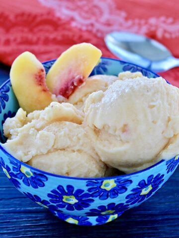 Two scoops of healthy peach frozen yogurt and two peach slices in a blue bowl.