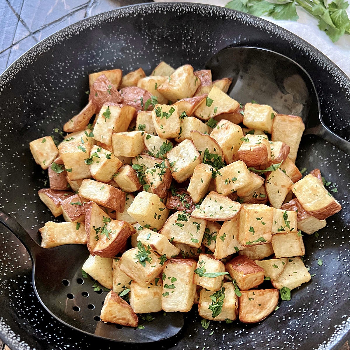 Air fryer diced potatoes in a black bowl with two black spoons.
