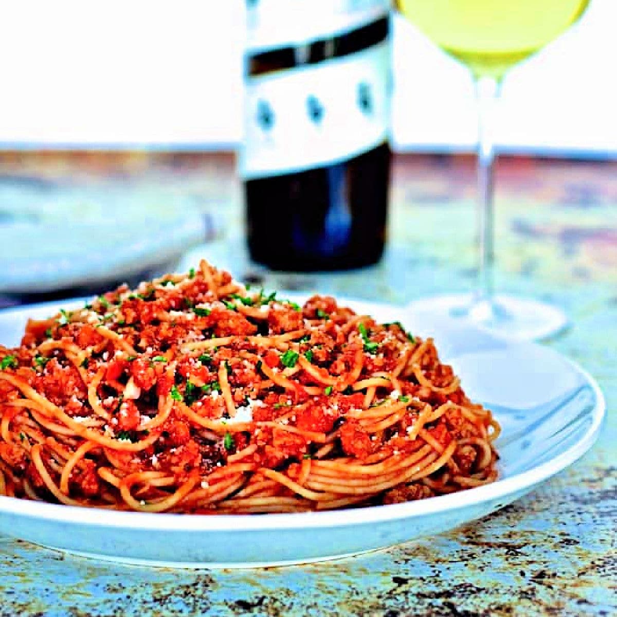 Spaghetti with healthy turkey bolognese sauce in a white bowl with a bottle and glass of white wine in the background.