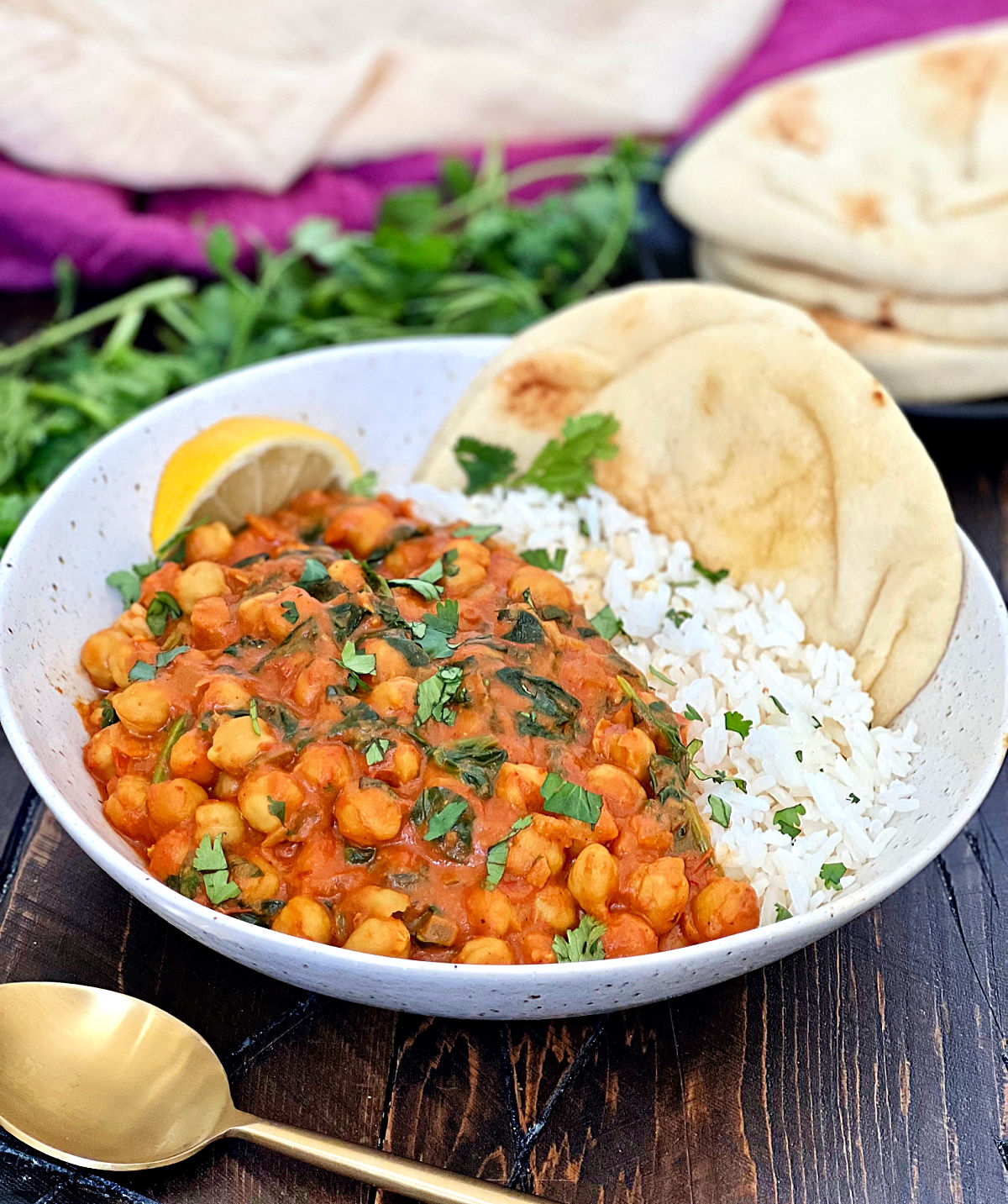 A white bowl with chickpea spinach curry and white rice with naan bread.