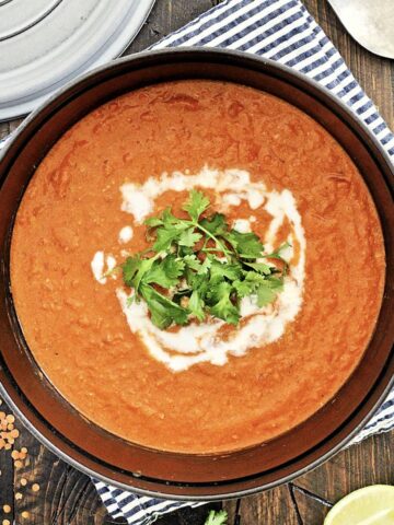 Overhead photo of red lentil coconut soup in a pot garnished with yogurt and cilantro.