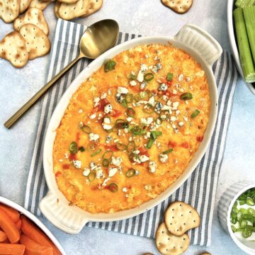 Healthy Buffalo chicken dip in an oval dish with vegetables and crackers around it.