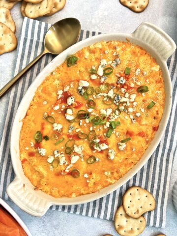 Healthy Buffalo chicken dip in an oval dish with vegetables and crackers around it.