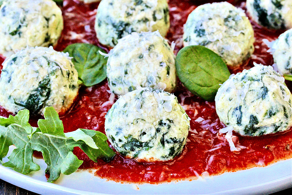 Spinach gnudi on a plate of tomato sauce.