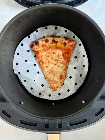 A slice of hot pizza in an air fryer basket.