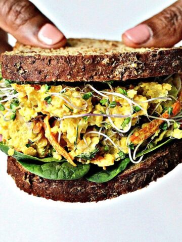Two hands holding a chickpea egg salad sandwich.