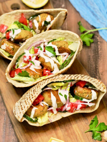 3 falafel pita sandwiches on wood board.