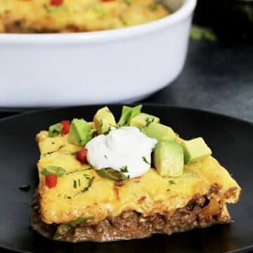 Piece of easy keto taco casserole on a black plate in front of a white casserole dish.