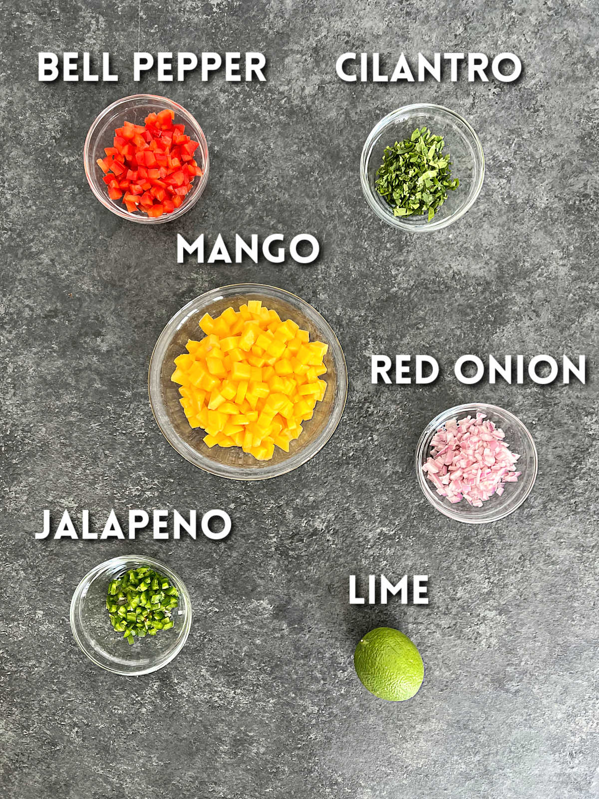 Ingredients for mango salsa on a gray board.