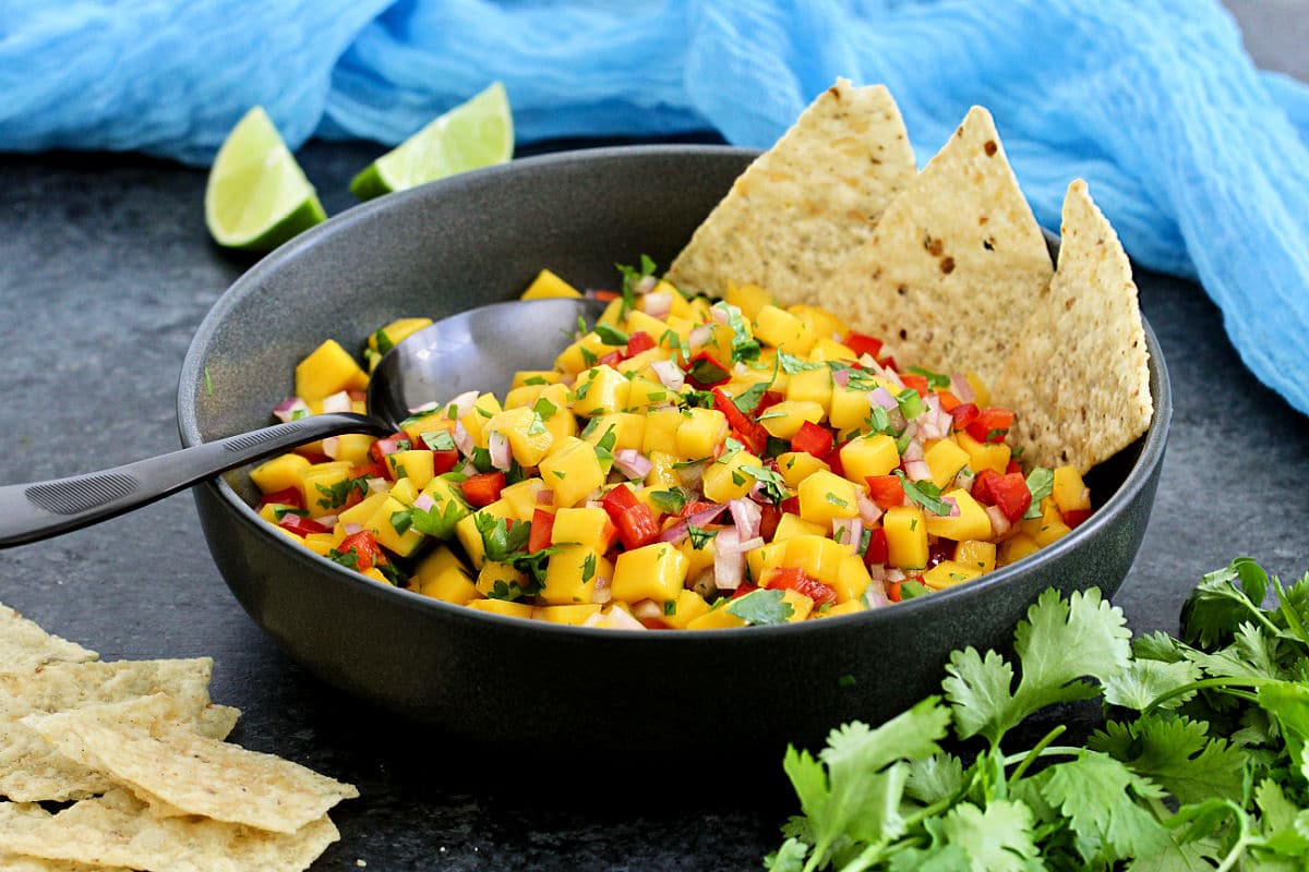 Mango salsa in a black bowl with tortilla chips.