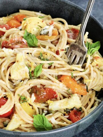 Close up of Mediterranean pasta in a gray bowl with a fork sticking in it.