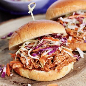 Two BBQ pulled chicken sandwiches on a wooden board.