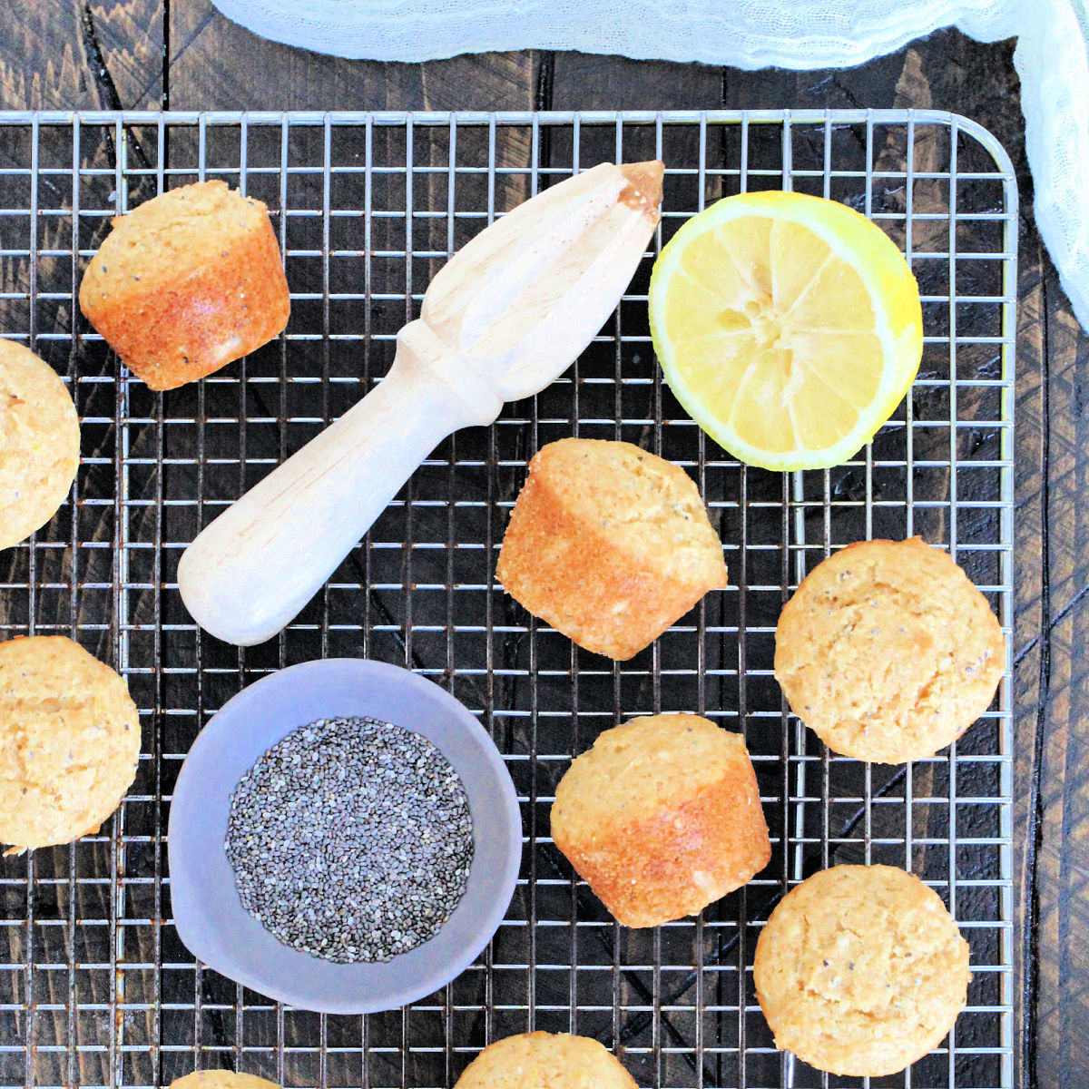 Lemon chia seed muffins on a baking rack with a bowl of chia seeds and a cut lemon.