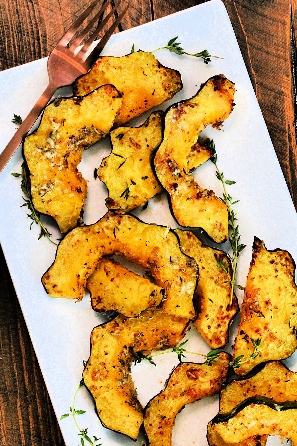 Slices of air fryer acorn squash garnished with fresh thyme on a white platter with a bronze fork.