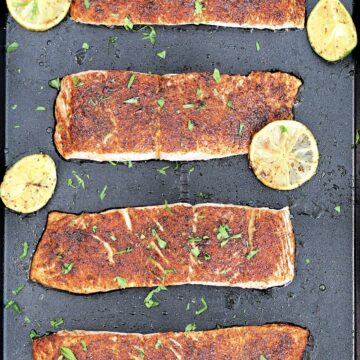 Four fillets of Low Sodium Chile Lime Salmon on a black baking sheet with limes slices around them.