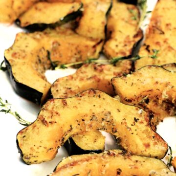 Slices of air fryer acorn squash garnished with fresh thyme on a white platter.