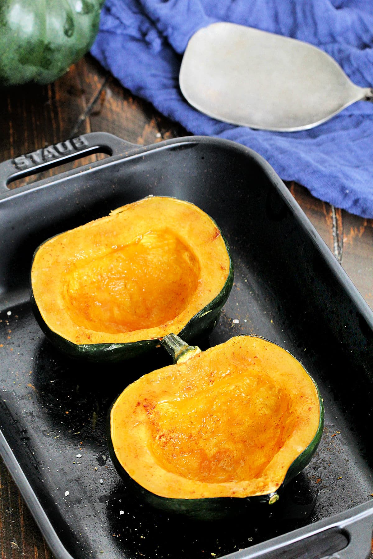 Microwaved acorn squash in a black baking dish with a blue napkin and metal serving spoon nearby.