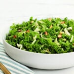 A copycat recipe of Chick-fil-A kale crunch salad in a white bowl with a blue striped napkin and gold fork around it.