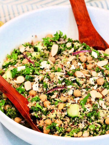 A quinoa and kale salad in a white bowl with a wooden serving spoon and fork.