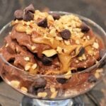 Healthy chocolate banana "ice cream" in a glass bowl topped with peanut butter, chocolate chips and crushed peanuts.