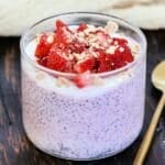 Strawberry cheesecake chia pudding in a glass topped with fresh strawberries and crumbled graham crackers.