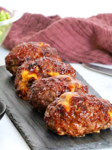 Side view of barbecue cheddar mini meatloaves on slate board with bowl of broccoli nearby.
